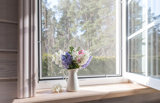 White window with a mosquito net in a rustic wooden house. Spring bouquet of hyacinths on the windowsill