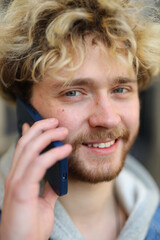 Close-up of a curly-haired young guy talking on the phone.