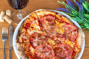 Frische hausgemachte italienische Pizza Salami mit einem Glas Wein an einem dekorierten Tisch