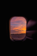 A spectacular view of a brilliant orange and pink sunset as seen through an airplane window, with distant airfield lights creating a tranquil atmosphere. Captures the beauty of travel and evening skie