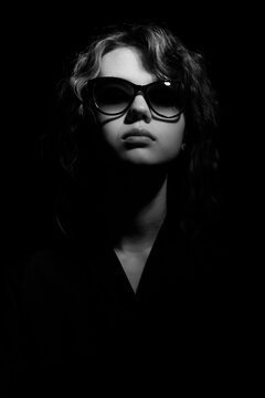 Fashionable portrait of a young woman in sunglasses in contrast lighting.