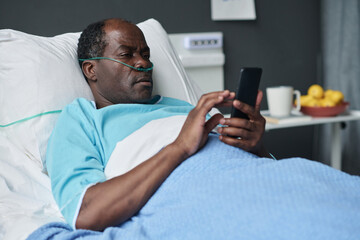 Obraz premium African American elderly patient using smartphone while lying on bed in hospital