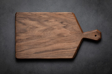 Walnut wood chopping board with handle. Handmade walnut wood cutting board on dark tone background.
