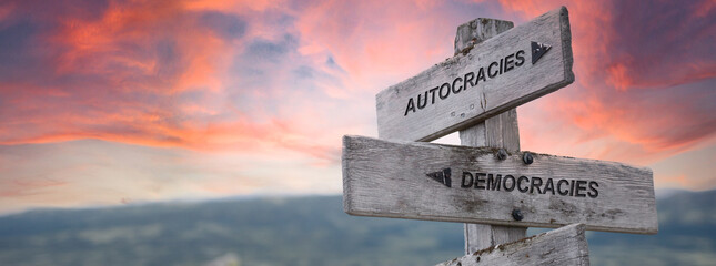 autocracies democracies text quote on wooden sign outdoors in nature. pink dramatic sunset...