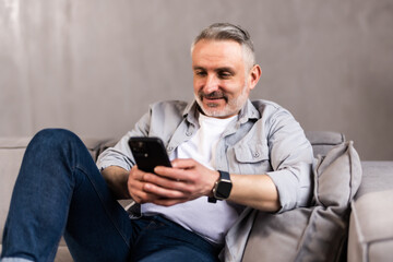 Older man at home, sitting on couch in living room, using phone, checking social media.