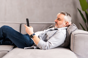 Handsome bald man is lying on the couch and reading something funny on his phone