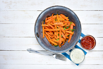 Homemade carrot chips in old antique bowl, silver fork, hot chilli and garlic sauce on white wooden desk. Top view.
