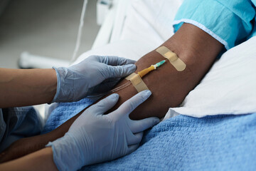 Close-up of nurse inserting catheter in arm of patient while he lying on bed in ward