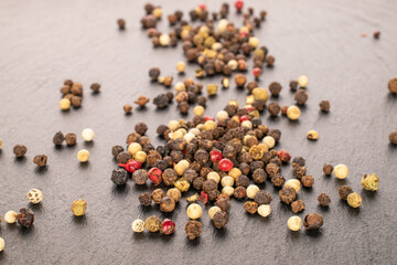 A mixture of four peppercorns, on slate stone.