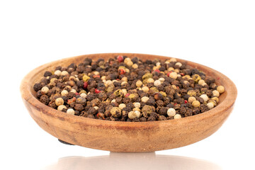 A mixture of four peppercorns on a wooden saucer, macro, isolated on a white background.