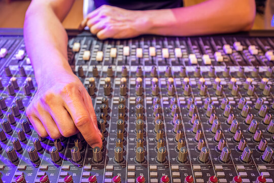 sound engineer hand tweaking EQ knob on audio mixing console in recording, broadcasting studio