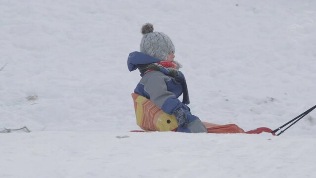 Little kid on sleigh pulled by parent on snow