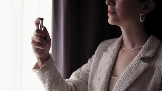 Stylish young business woman in formal wear with pearl accessories, necklace and earrings getting ready at home for work, puttin on perfume. Beauty, style, morning routine