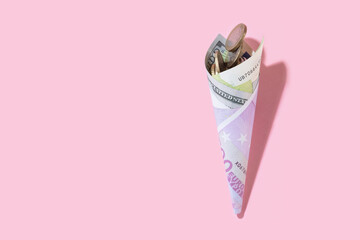 Roll of money. Horn from dollar, coins and euro banknotes on a pink background with copy space....