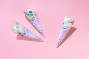 Rolls of money. Three horn from dollar and euro banknotes on a pink background with copy space....