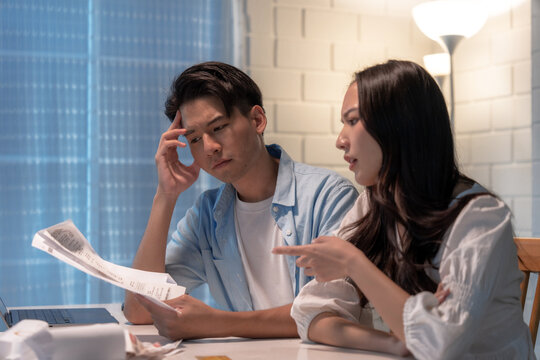 Stressed And Confused Asian Couple Calculating Expenses On Invoices.