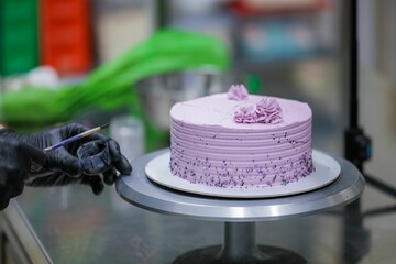 Baker wearing protective gloves decorating a beautiful purple cake in the kitchen