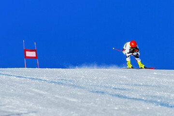 ski racer on alpine skiing track downhill, red gate and snowy slope on blue sky background, winter...