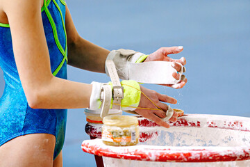 close-up hands girl gymnast in gymnastics grips apply gym chalk from magnesia stands on blue...