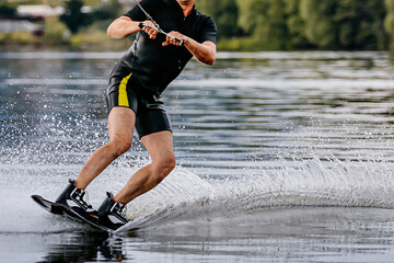 male athlete wakesurfing behind motorboat on pond, extreme summer water sports