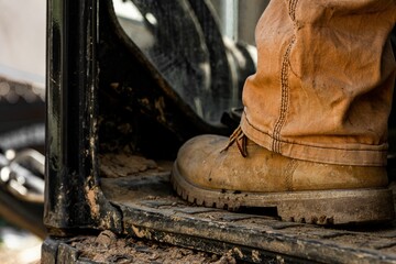 Close-up shot of brown leather boot of a construction worker sitting on an aged dirty tractor