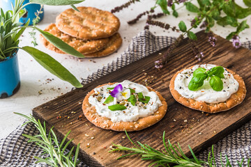 Round crispbread with herbal cream cheese and fresh herbs on a wooden board