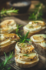 Baguette bread slices baked with goat cheese and honey on wooden background, vertical closeup