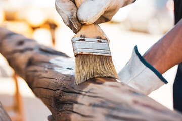 A faceless master carpenter works with wood by treating a surface with glue to protect it from...