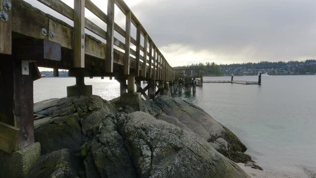 Wooden Quay on a rocky beach in Indian Arm, Vancouver, British Columbia, Canada. Belcarra Pier, West Coast of Pacific Ocean. Spring Season Sunny Cloudy Evening. Slow Motion