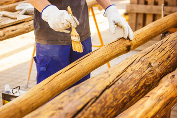 A faceless master carpenter works with wood by treating a surface with glue to protect it from insects. Carpentry work holding a brush. Products made of wood. Logs of trees Wood staining, woodworking