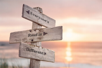 everyones road is different text quote written on wooden signpost at the beach during sunset. - obrazy, fototapety, plakaty