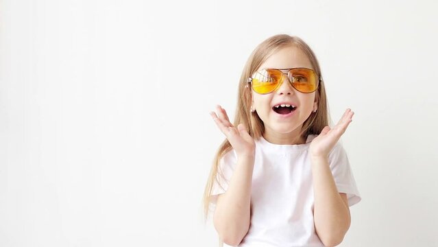 little girl in yellow glasses and a white T-shirt smiling on a white background