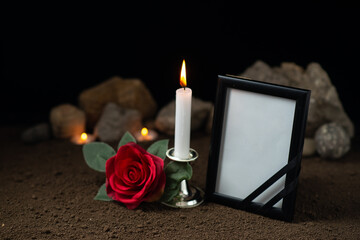 burning candle with empty picture frame and red rose on dark desk sci fi death