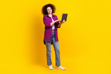 Full length photo of adorable shiny woman dressed plaid shirt typing modern device isolated yellow color background