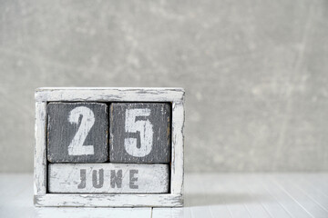 Calendar for June 25, made wooden cubes, against light concrete wall.With an empty space for your...