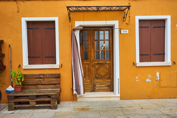 Door and windows with flowers on the yellow facade of the house. Colorful architecture in Burano island, Venice.