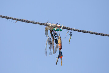 Tangled fishing line and lures wrapped around overhead wires against a blue sky near a river