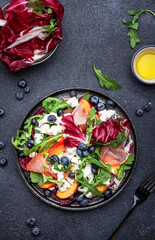 Delicious salad  with arugula, radicchio, peaches, prosciutto, feta cheese and blueberries. Black table background, top view