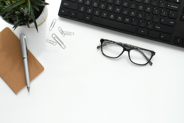 Business background concept - white desktop black keyboard notebook pen plant - flat lay copy space