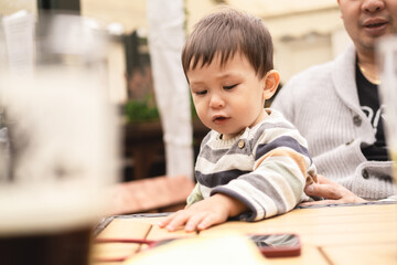 Male infant looking down touching the wooden table with his hand sitting on father's legs at a table in a beer garden in a pub in Edinburgh, Scotland. Multiracial multicultural family.