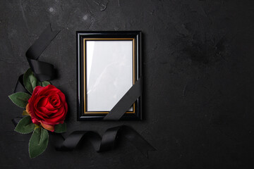 top view of black bow with red flower and picture frame on dark background funeral death