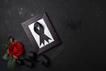 top view of picture frame with black bow and red flower on a dark surface death funeral