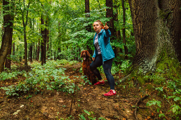 Young beautiful woman runs with Irish Setter dog that pulls on a leash and laughs through colorful spring forest.