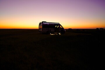 Fototapeta na wymiar Silhouette of a small camper parked in a beautiful open landscape at sunset