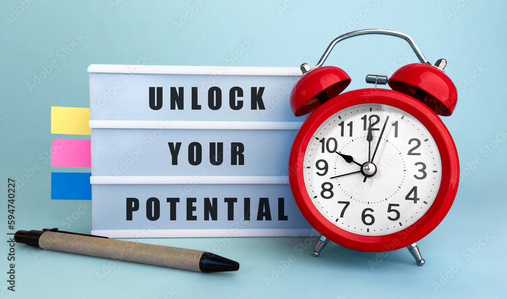 Poster text unlock your potential written on the lightbox with alarm clock and colorfull stickers on blue b