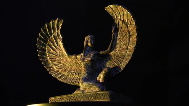 Close-up of the goddess Isis. Female winged egyptian goddess minifigure illuminated with warm yellow light over black background. The shot was made on a rotating platform. The footage can be looped.