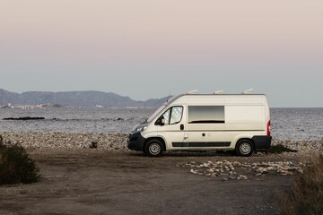 Fototapeta na wymiar White van parked on the beach with a tranquil sea in the background