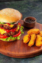 Tasty sandwich and chicken nuggets on brown wooden cutting board on ice background with free space