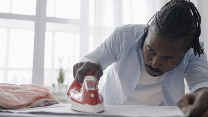 African American man perfectionist meticulously ironing clothes, household chores