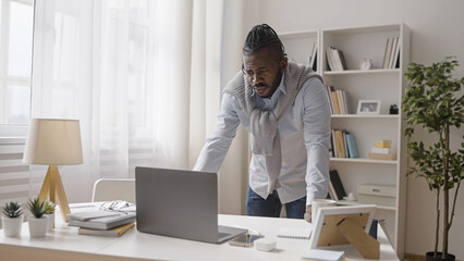 Concentrated man is looking at his laptop display, working on a difficult project